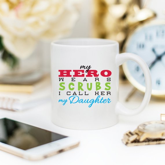 Funny Nurse Mug featuring the phrase 'My Hero Wears Scrubs, I Call Her My Daughter', perfect for coffee lovers.