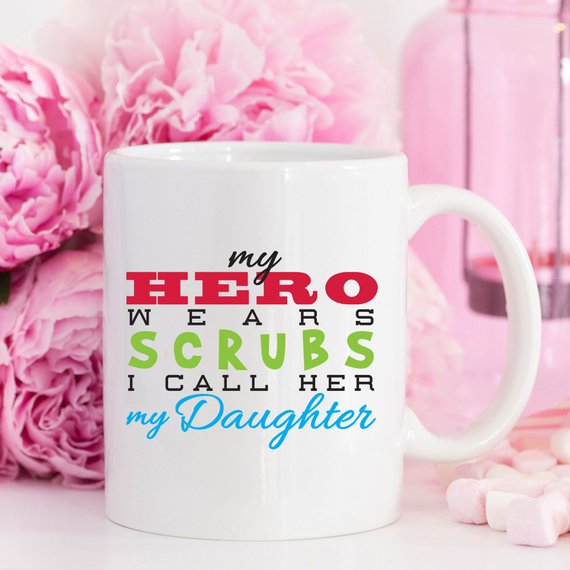 Funny Nurse Mug featuring the phrase 'My Hero Wears Scrubs, I Call Her My Daughter', perfect for coffee lovers.