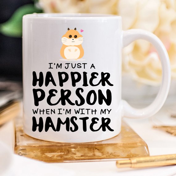 A humorous coffee mug featuring a hamster design with the text 'I'm Just A Happier Person When I'm With My Hamster', made of high-quality ceramic.