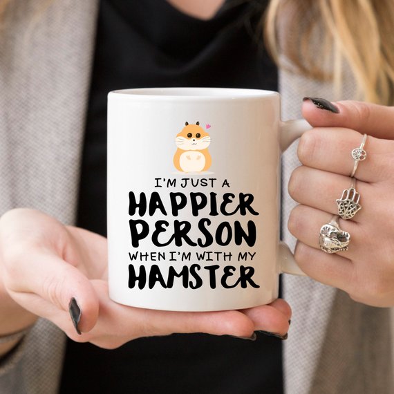 A humorous coffee mug featuring a hamster design with the text 'I'm Just A Happier Person When I'm With My Hamster', made of high-quality ceramic.