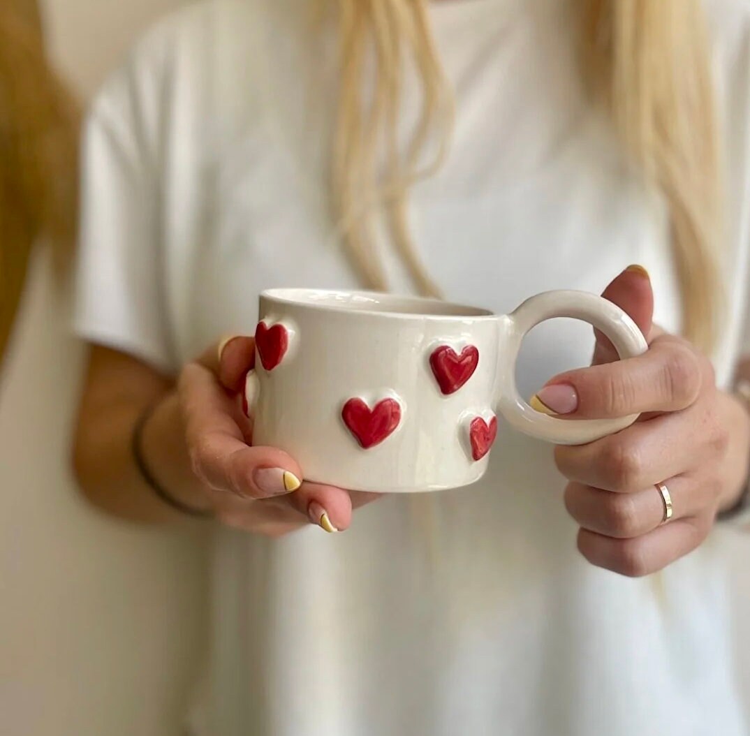 Handmade ceramic coffee mug with a small red heart design, showcasing artisan craftsmanship and vibrant colors.