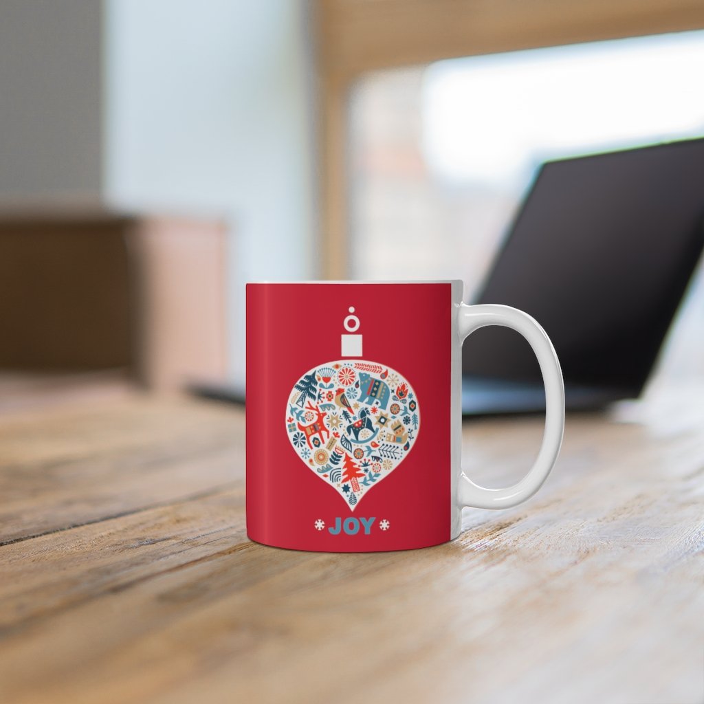 Holiday Ornament with Joy ceramic mug featuring a red backdrop and joyful design, perfect for hot beverages.