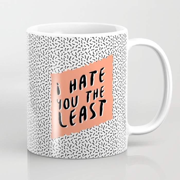 A humorous ceramic coffee mug with the phrase 'I Hate You the Least' printed in a playful font, featuring a wrap-around design and a large handle for easy gripping.