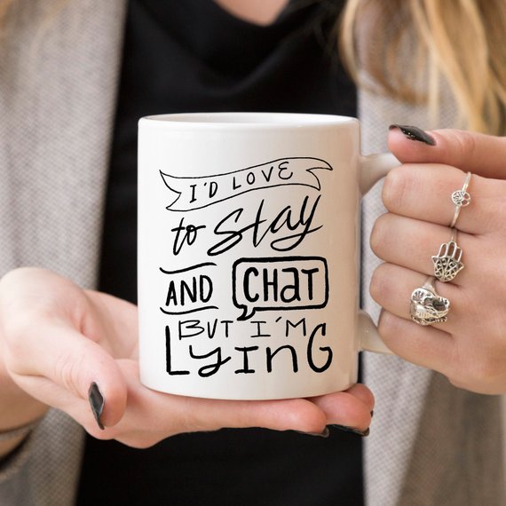 A humorous ceramic coffee mug featuring the phrase 'I'd Love To Stay And Chat But I'm Lying', showcasing its dishwasher and microwave safe design.