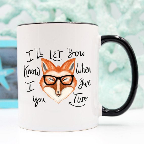 A humorous coffee mug featuring the phrase 'I'll Let You Know When I Give Two Fox', designed for coffee lovers.