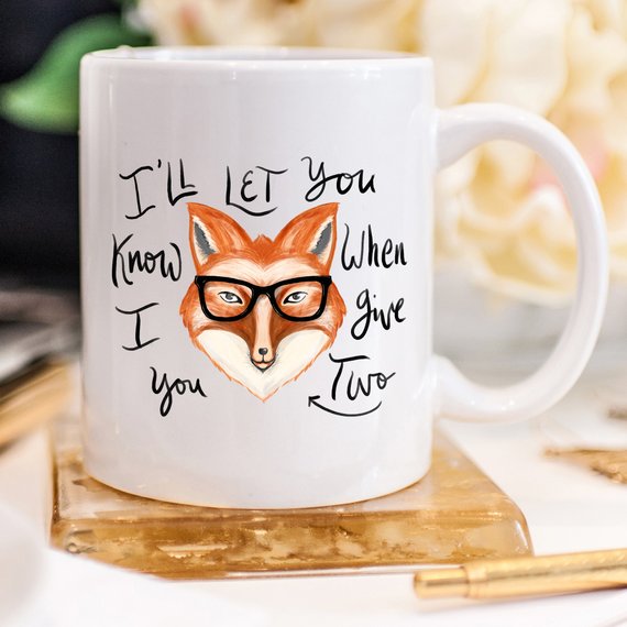 A humorous coffee mug featuring the phrase 'I'll Let You Know When I Give Two Fox', designed for coffee lovers.