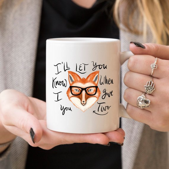 A humorous coffee mug featuring the phrase 'I'll Let You Know When I Give Two Fox', designed for coffee lovers.