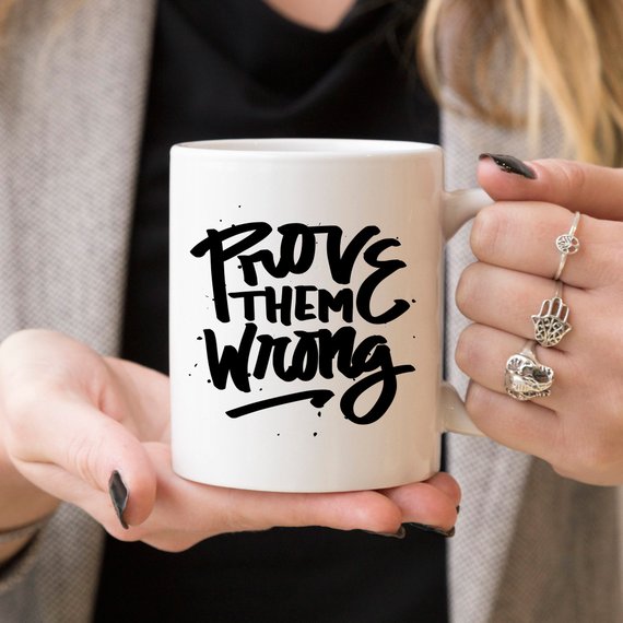 A white ceramic coffee mug with the phrase 'Prove Them Wrong' printed in bold letters, showcasing a motivational and humorous design.