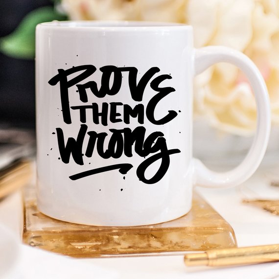 A white ceramic coffee mug with the phrase 'Prove Them Wrong' printed in bold letters, showcasing a motivational and humorous design.