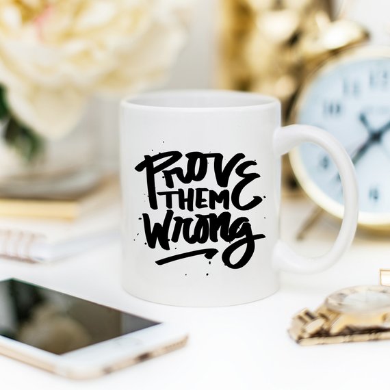 A white ceramic coffee mug with the phrase 'Prove Them Wrong' printed in bold letters, showcasing a motivational and humorous design.