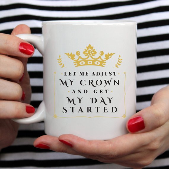 A humorous coffee mug with the phrase 'Let Me Adjust My Crown And Get My Day Started' printed on it, showcasing a fun and motivational design.