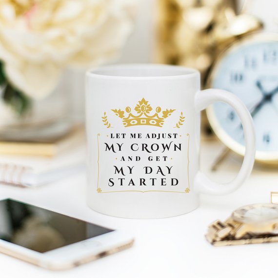 A humorous coffee mug with the phrase 'Let Me Adjust My Crown And Get My Day Started' printed on it, showcasing a fun and motivational design.