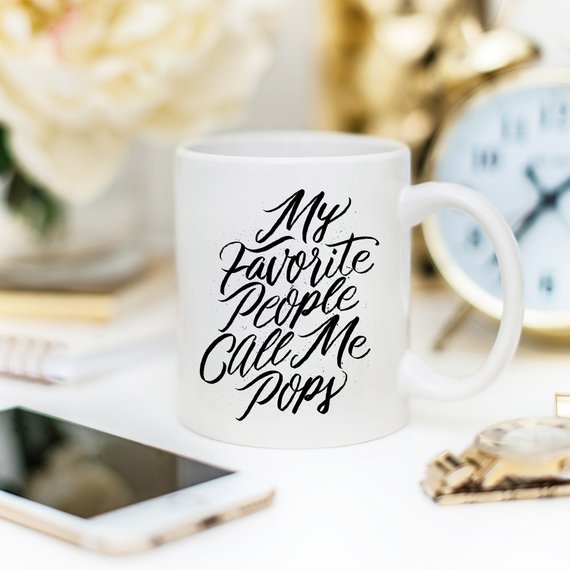 A white ceramic coffee mug with the text 'My Favorite People Call Me Pops' printed in a fun font, perfect for gifting.