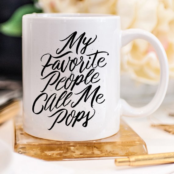 A white ceramic coffee mug with the text 'My Favorite People Call Me Pops' printed in a fun font, perfect for gifting.