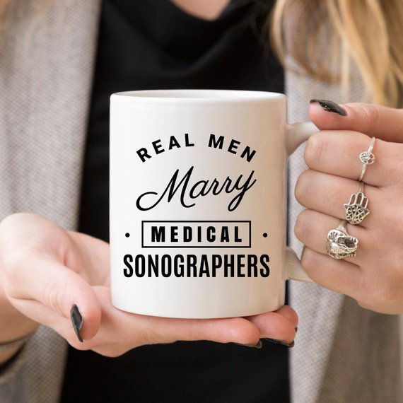 A humorous coffee mug featuring the phrase 'Real Men Marry Medical Sonographers', showcasing a fun design perfect for gifts.