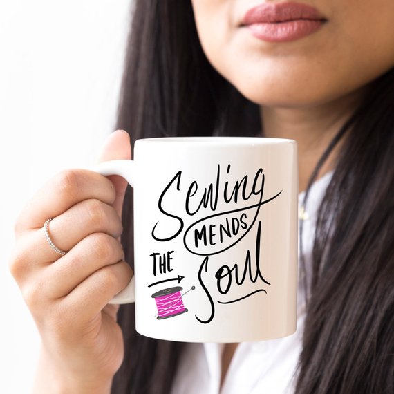 A ceramic coffee mug with the phrase 'Sewing Mends The Soul' printed in a fun design, perfect for sewing enthusiasts.