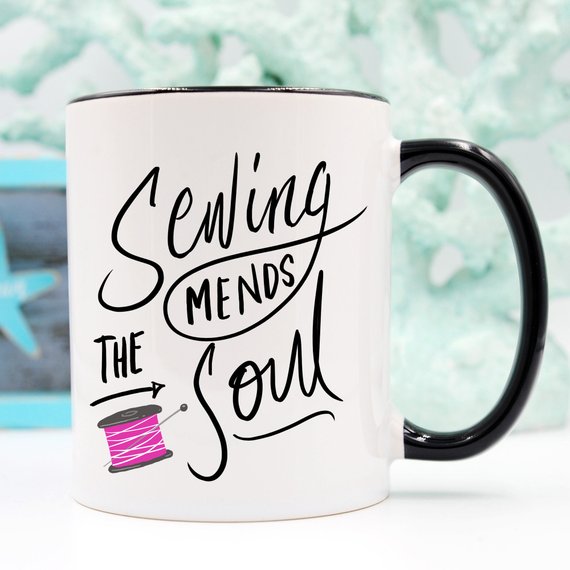 A ceramic coffee mug with the phrase 'Sewing Mends The Soul' printed in a fun design, perfect for sewing enthusiasts.