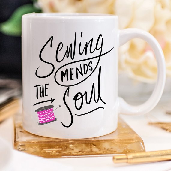 A ceramic coffee mug with the phrase 'Sewing Mends The Soul' printed in a fun design, perfect for sewing enthusiasts.