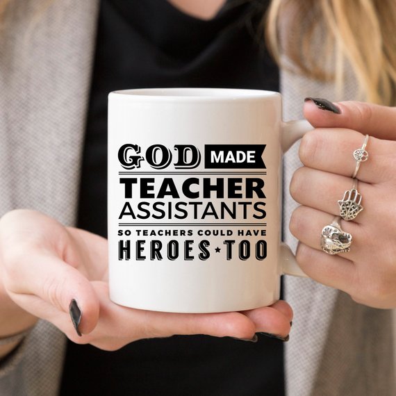 A white ceramic coffee mug with the text 'God Made Teacher Assistants So Teachers Could Have Heroes Too' printed in colorful letters, perfect for teacher assistants.