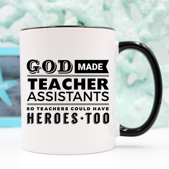 A white ceramic coffee mug with the text 'God Made Teacher Assistants So Teachers Could Have Heroes Too' printed in colorful letters, perfect for teacher assistants.