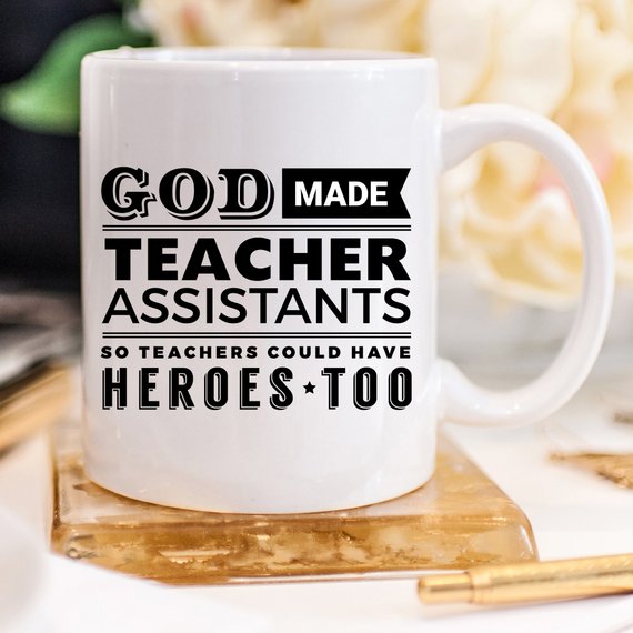 A white ceramic coffee mug with the text 'God Made Teacher Assistants So Teachers Could Have Heroes Too' printed in colorful letters, perfect for teacher assistants.