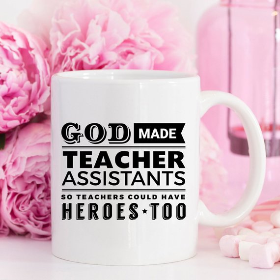 A white ceramic coffee mug with the text 'God Made Teacher Assistants So Teachers Could Have Heroes Too' printed in colorful letters, perfect for teacher assistants.