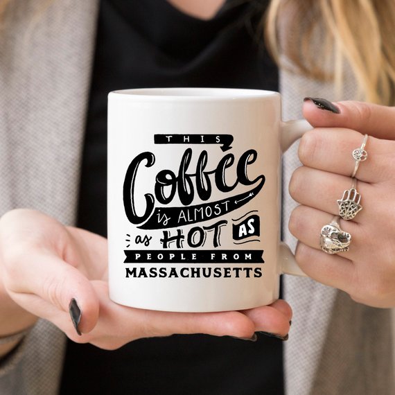 Funny coffee mug with the phrase 'This Coffee Is Almost As Hot As People From Massachusetts' printed on it, showcasing a humorous design.