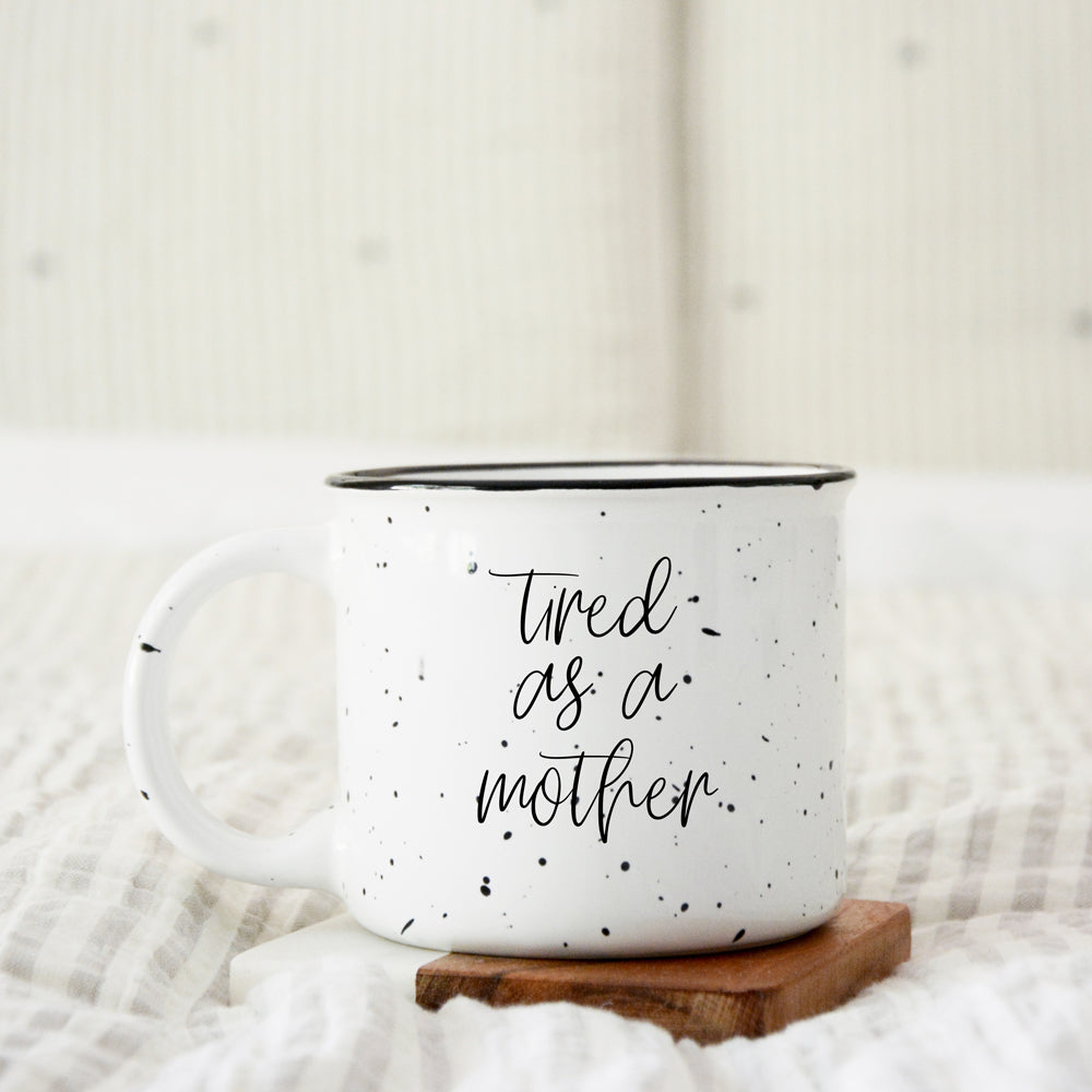 Tired as a Mother Campfire Mug with black rim and double-sided design, featuring white sesame glaze and bold black lettering.