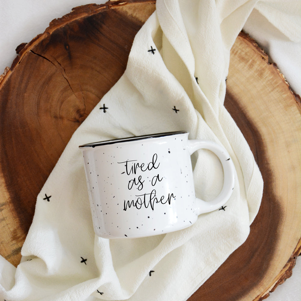 Tired as a Mother Campfire Mug with black rim and double-sided design, featuring white sesame glaze and bold black lettering.