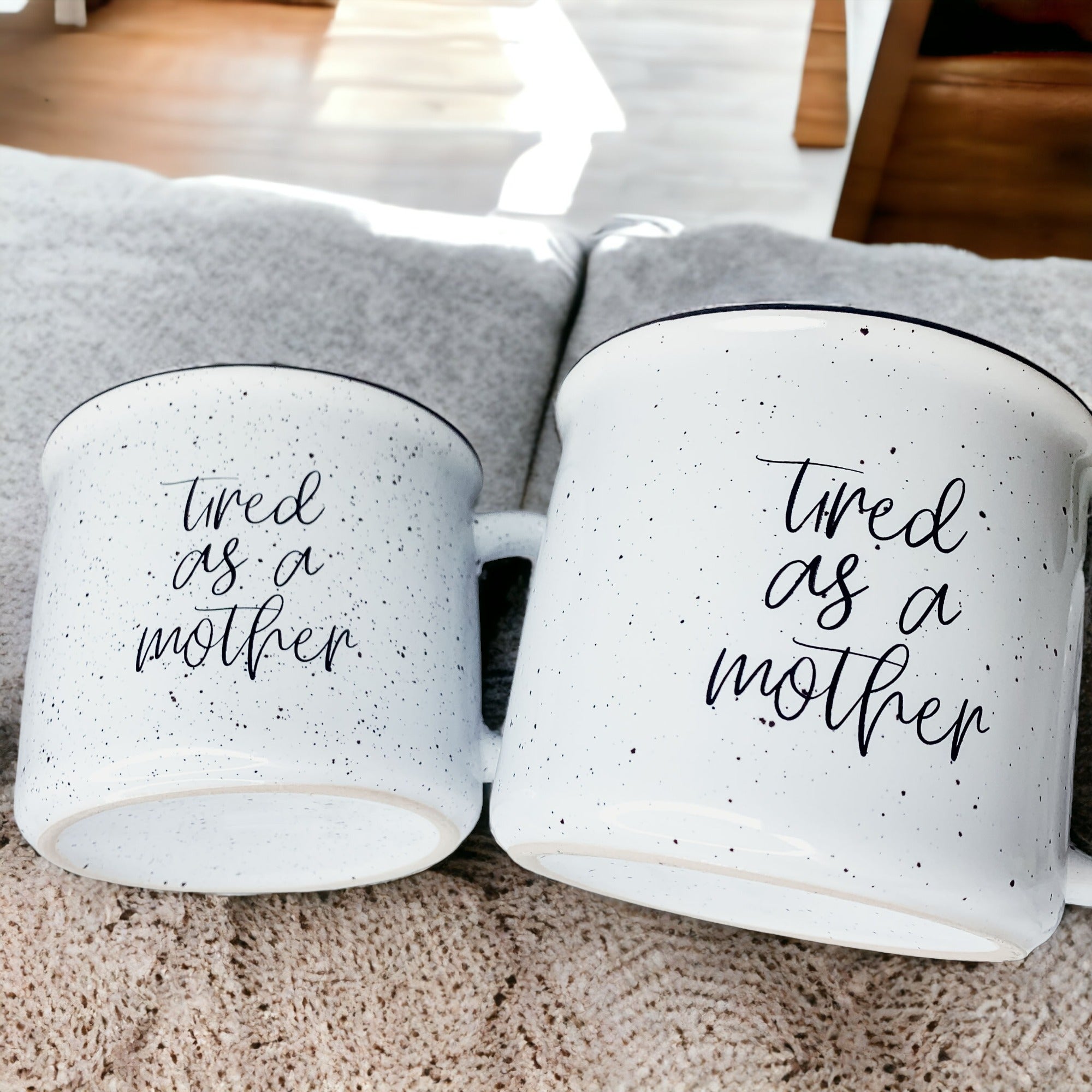 Tired as a Mother Campfire Mug with black rim and double-sided design, featuring white sesame glaze and bold black lettering.