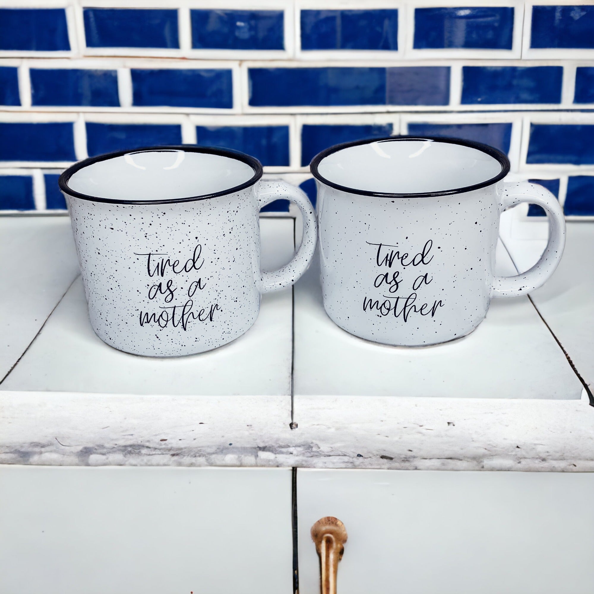 Tired as a Mother Campfire Mug with black rim and double-sided design, featuring white sesame glaze and bold black lettering.