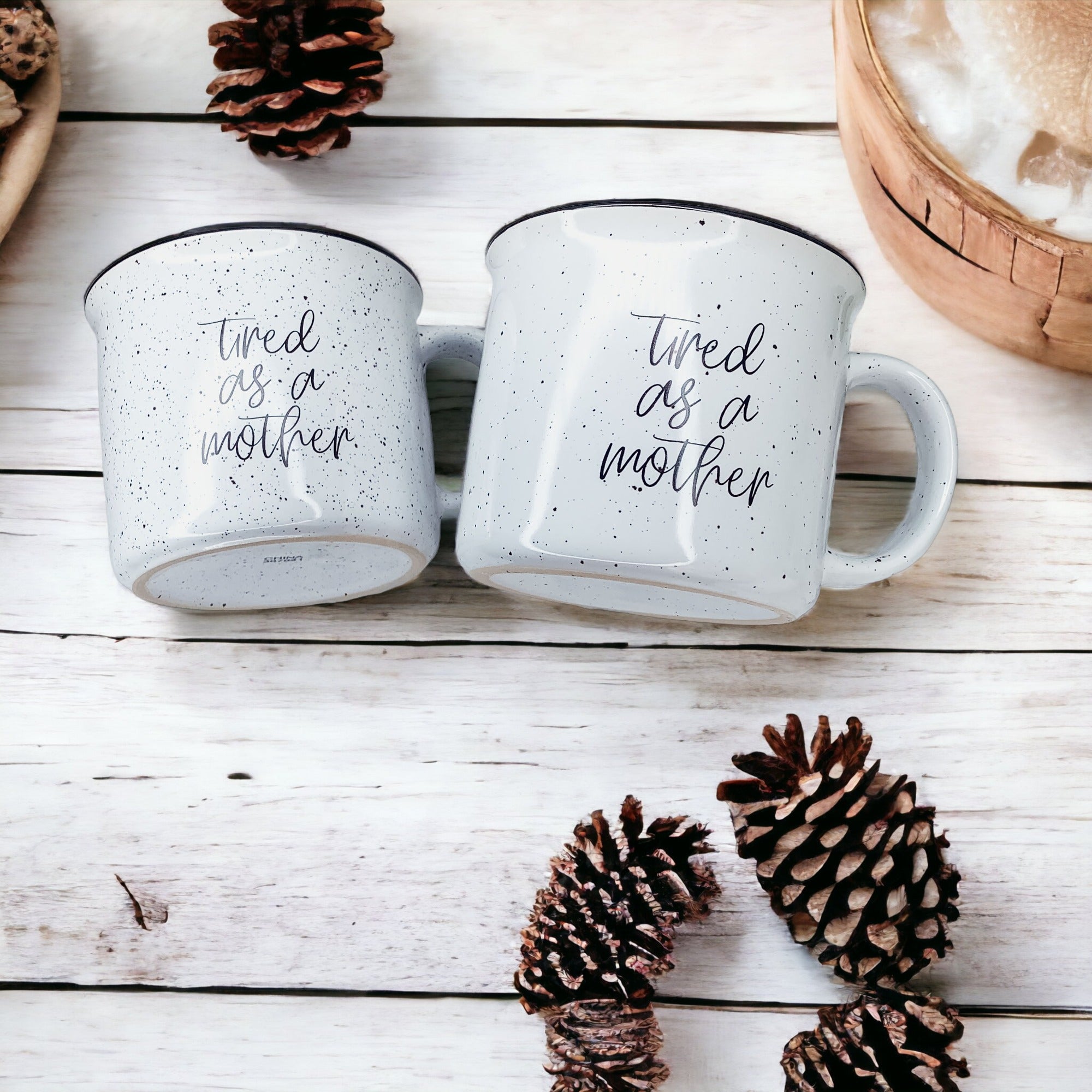 Tired as a Mother Campfire Mug with black rim and double-sided design, featuring white sesame glaze and bold black lettering.