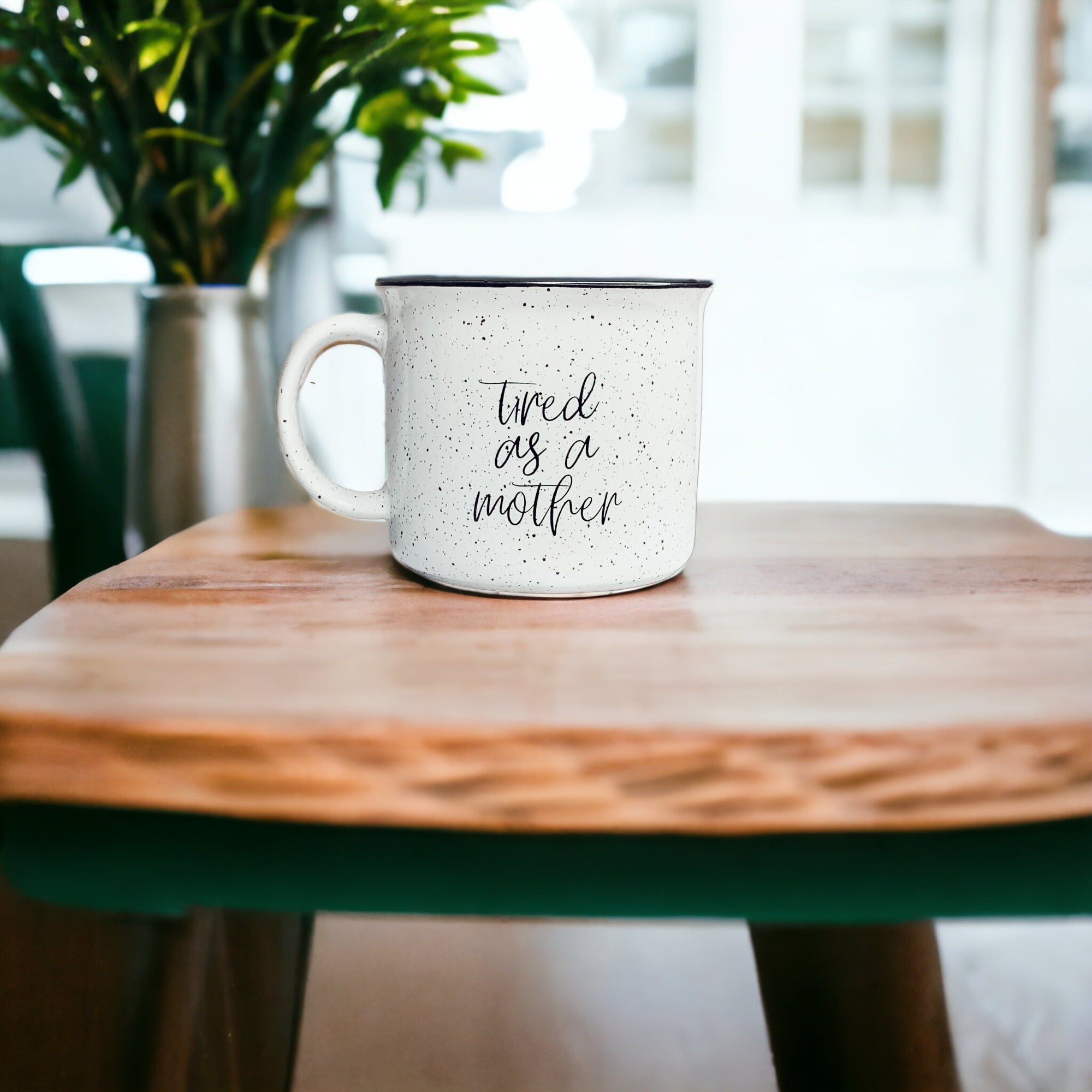 Tired as a Mother Campfire Mug with black rim and double-sided design, featuring white sesame glaze and bold black lettering.