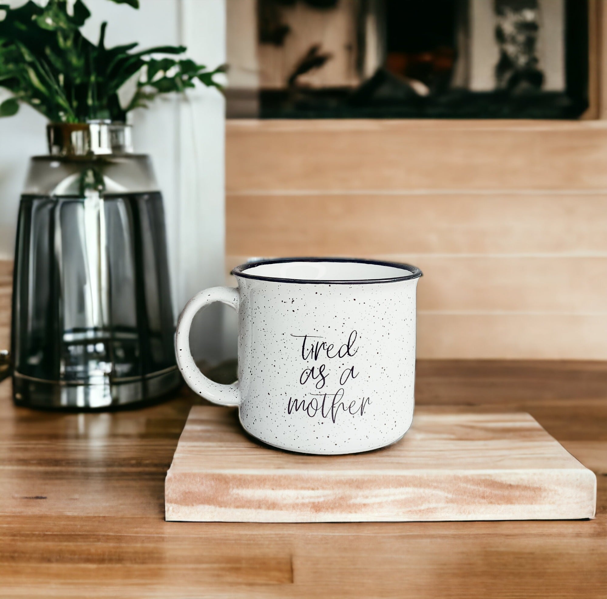 Tired as a Mother Campfire Mug with black rim and double-sided design, featuring white sesame glaze and bold black lettering.