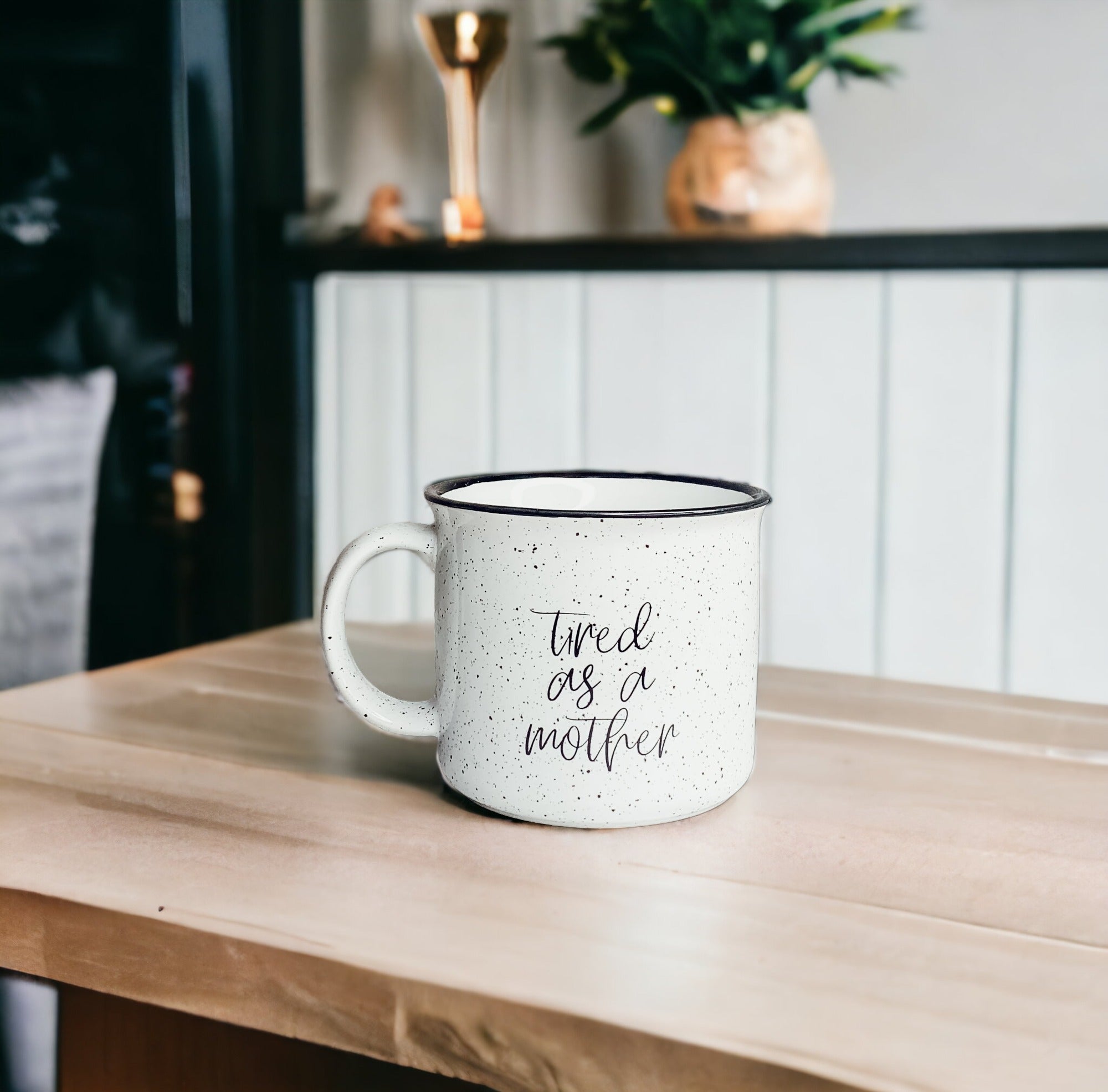 Tired as a Mother Campfire Mug with black rim and double-sided design, featuring white sesame glaze and bold black lettering.