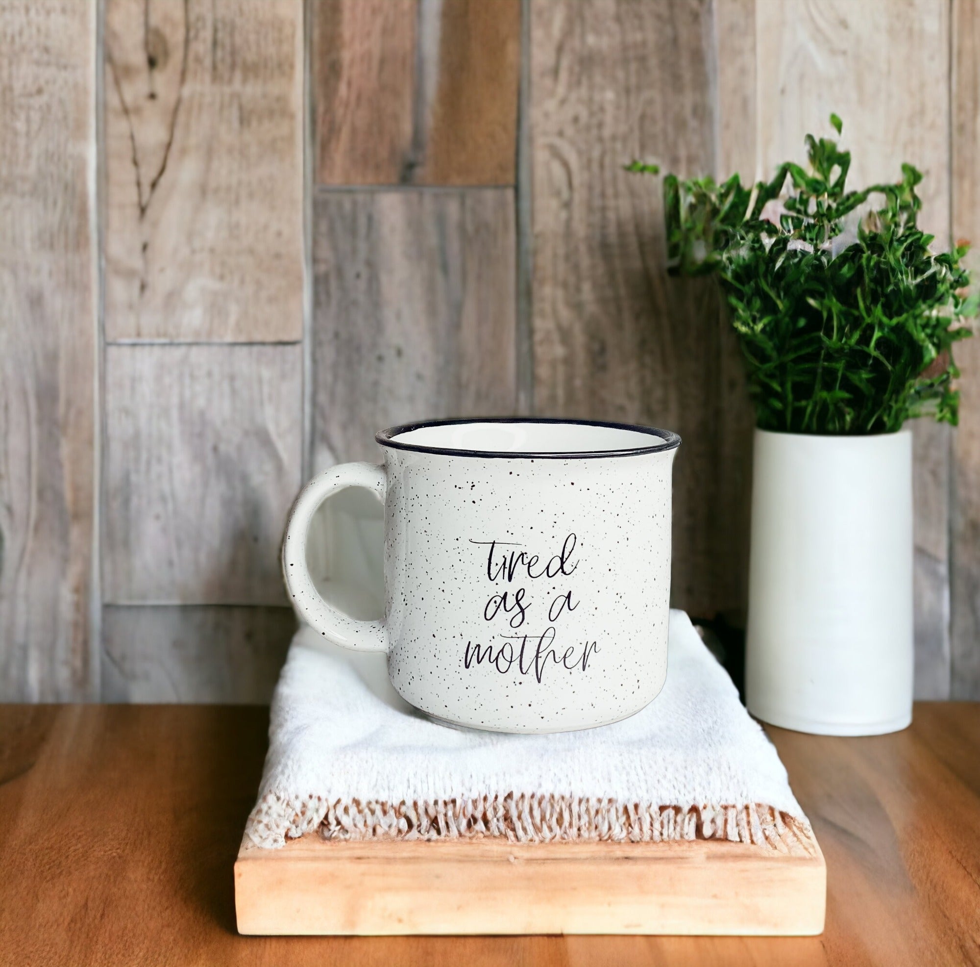 Tired as a Mother Campfire Mug with black rim and double-sided design, featuring white sesame glaze and bold black lettering.