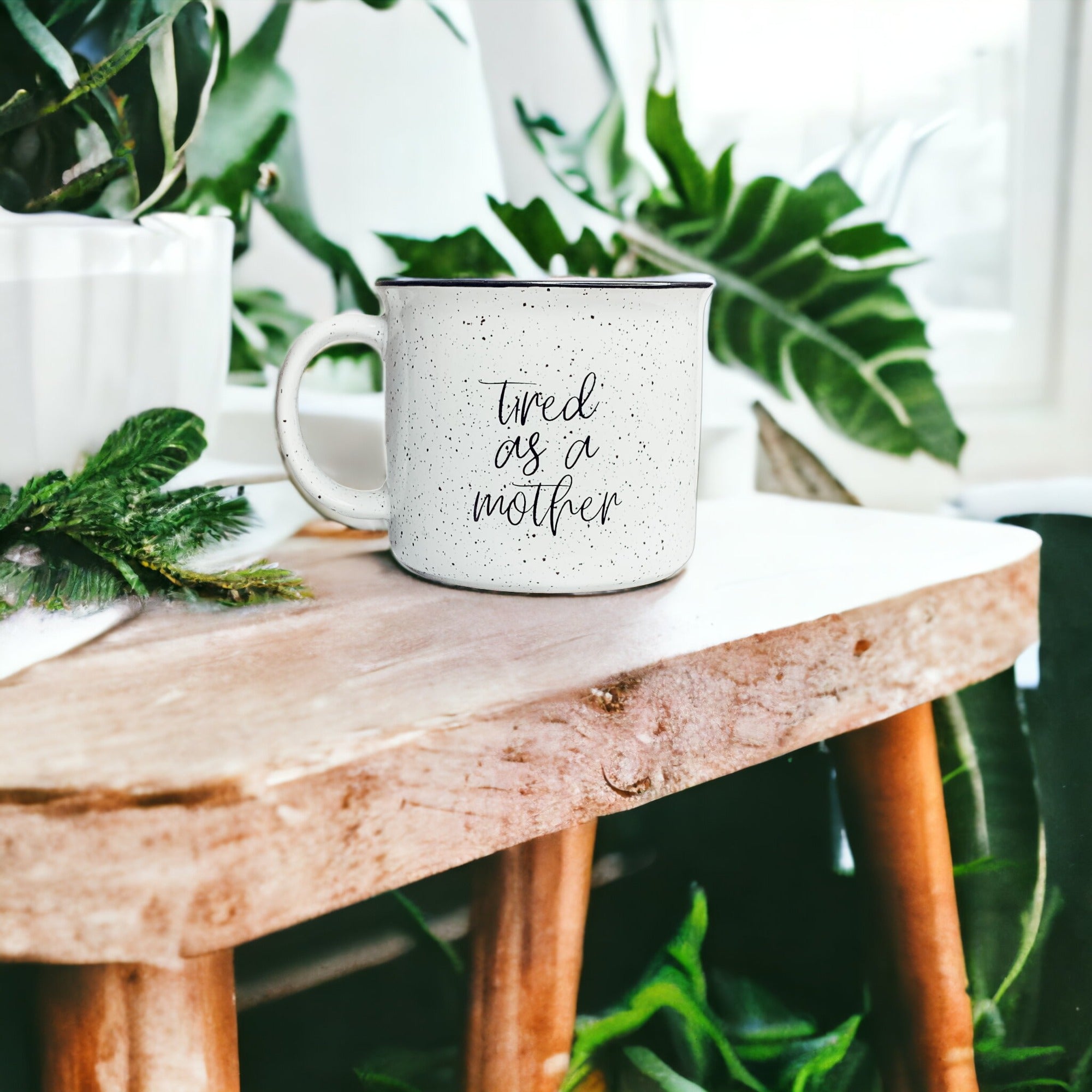 Tired as a Mother Campfire Mug with black rim and double-sided design, featuring white sesame glaze and bold black lettering.