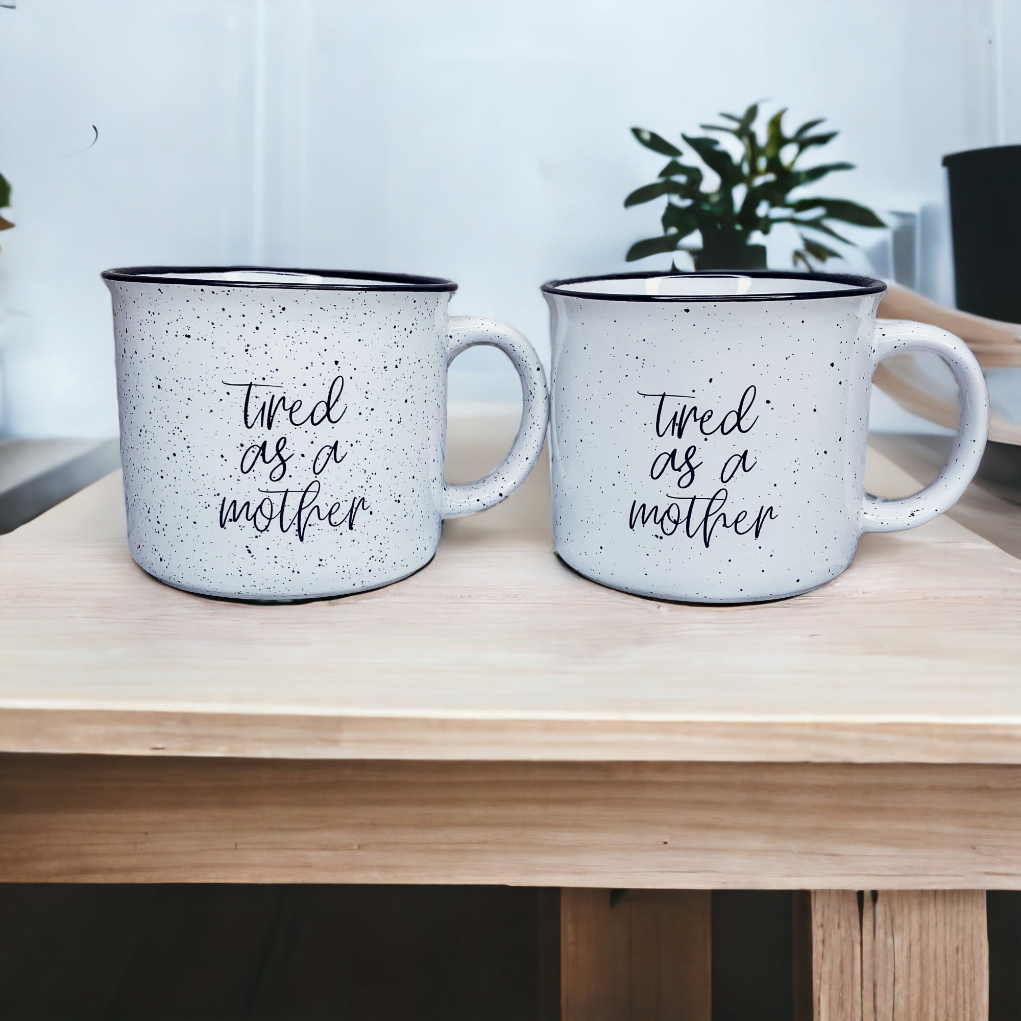 Tired as a Mother Campfire Mug with black rim and double-sided design, featuring white sesame glaze and bold black lettering.