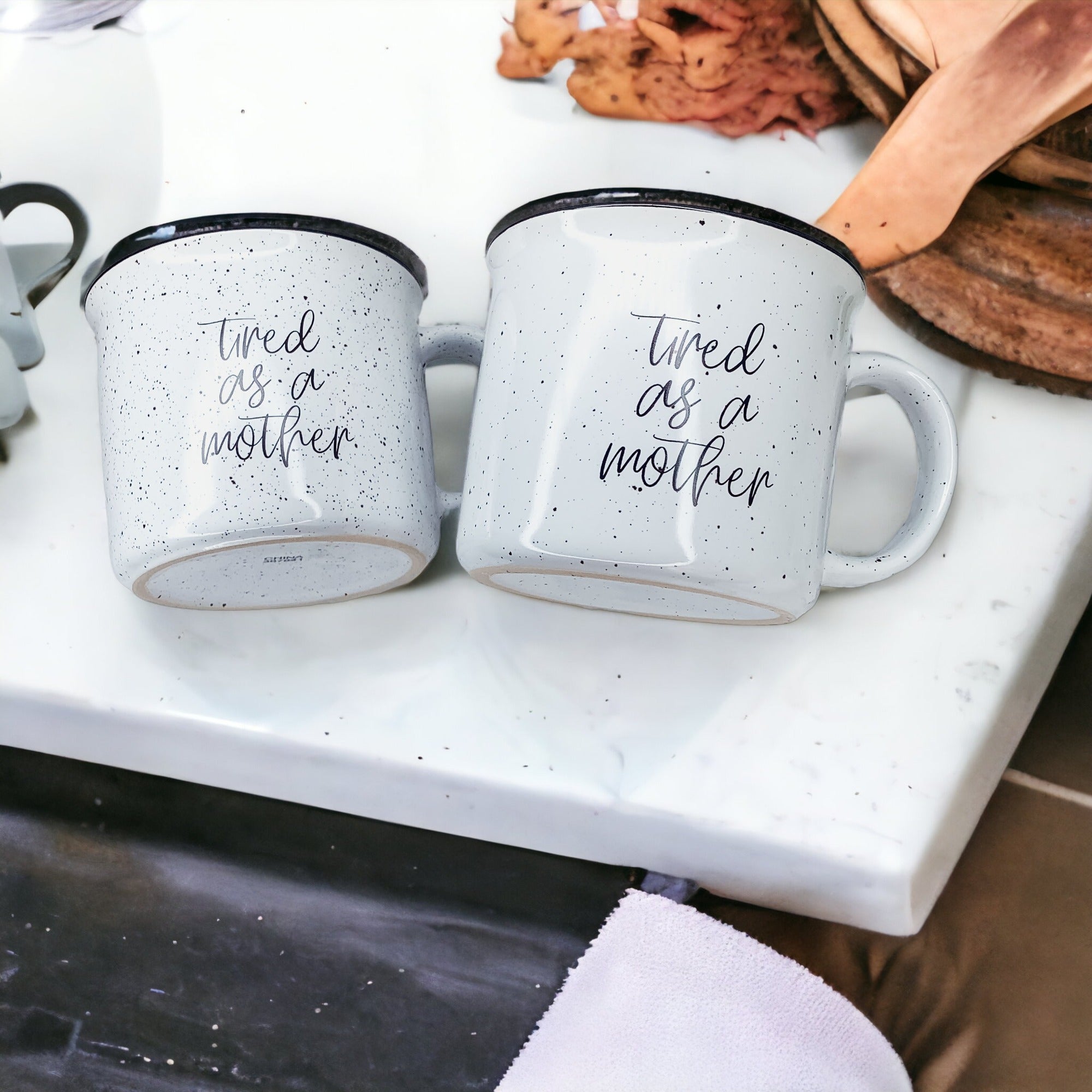 Tired as a Mother Campfire Mug with black rim and double-sided design, featuring white sesame glaze and bold black lettering.