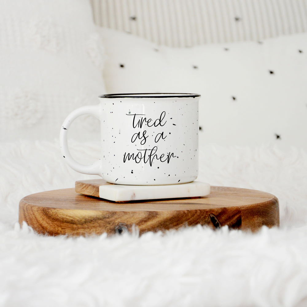 Tired as a Mother Campfire Mug with black rim and double-sided design, featuring white sesame glaze and bold black lettering.