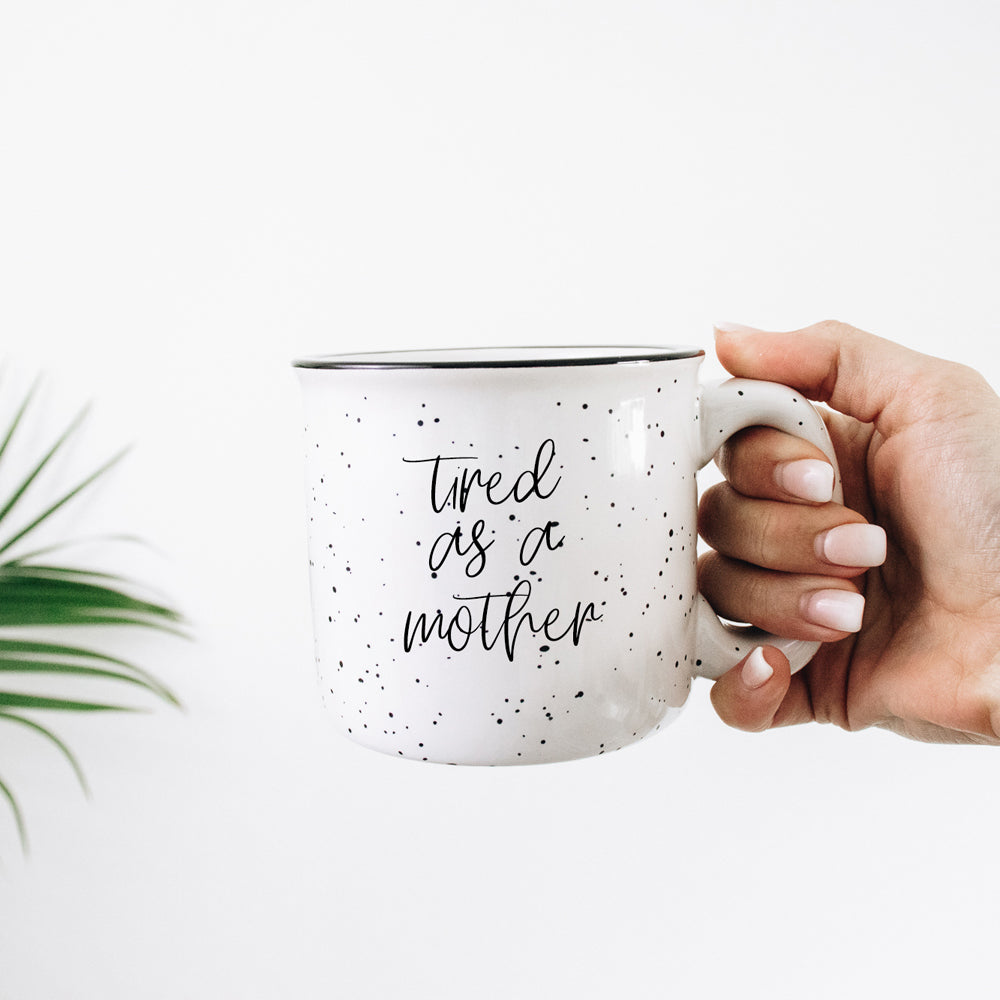 Tired as a Mother Campfire Mug with black rim and double-sided design, featuring white sesame glaze and bold black lettering.