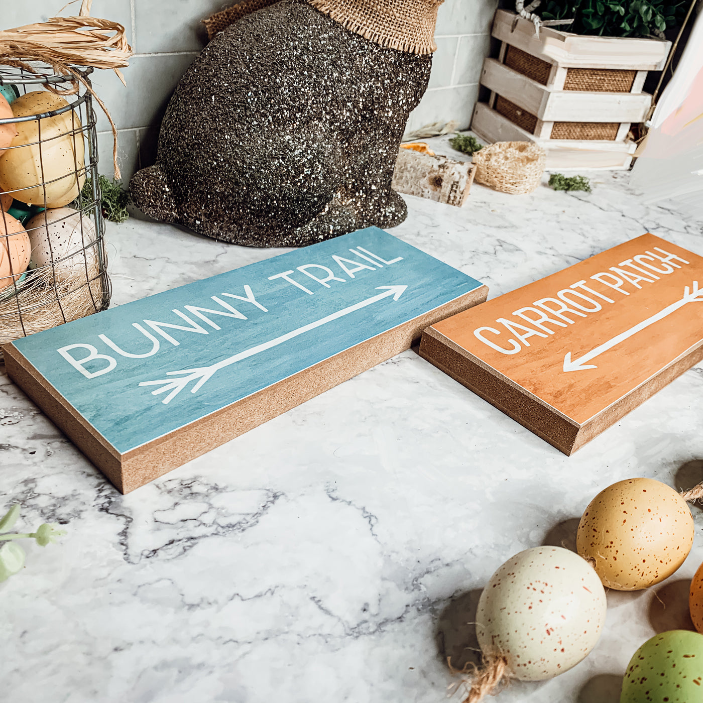 Two wooden block signs featuring Bunny Trail and Carrot Patch designs in pastel colors, perfect for Easter decor.