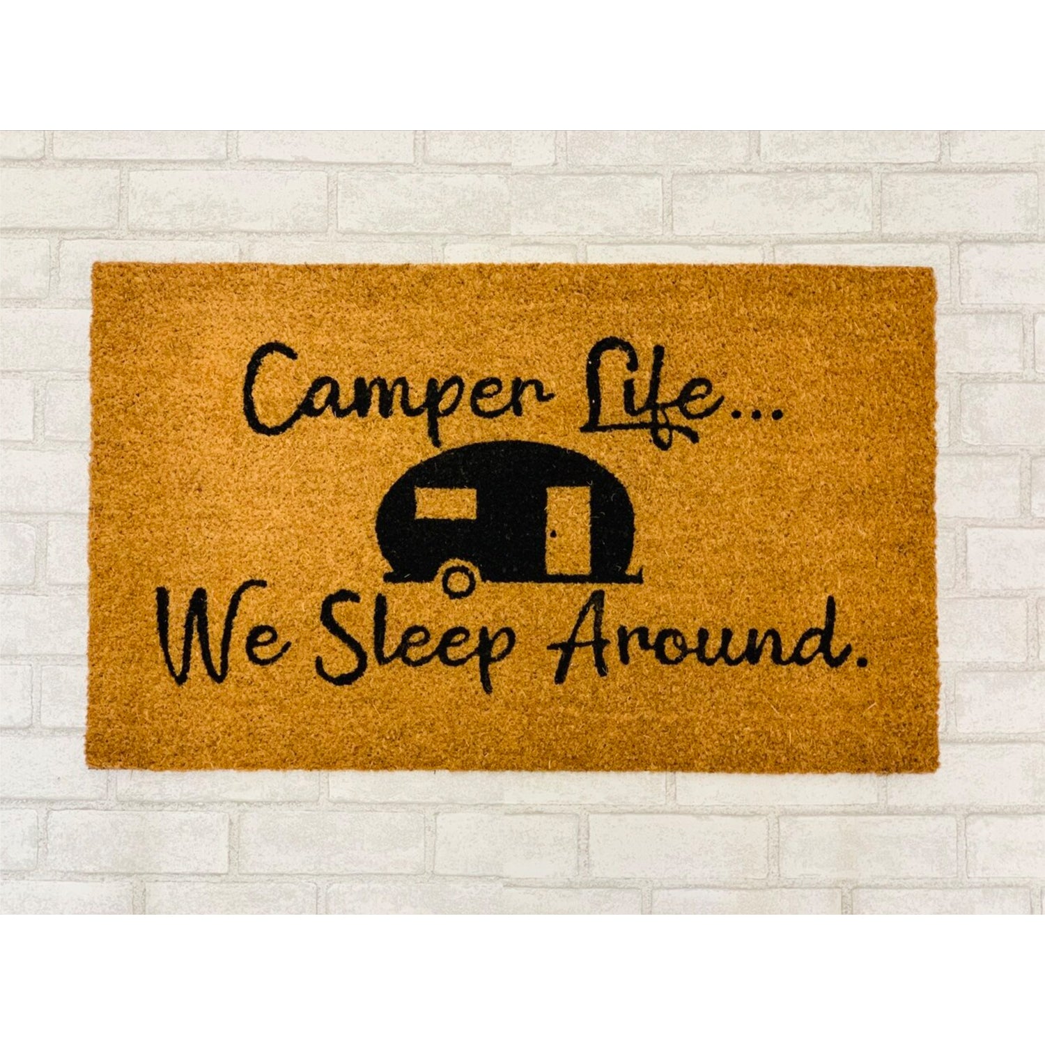 A humorous doormat with the phrase 'We Sleep Around', made of coir, perfect for camping entrances.