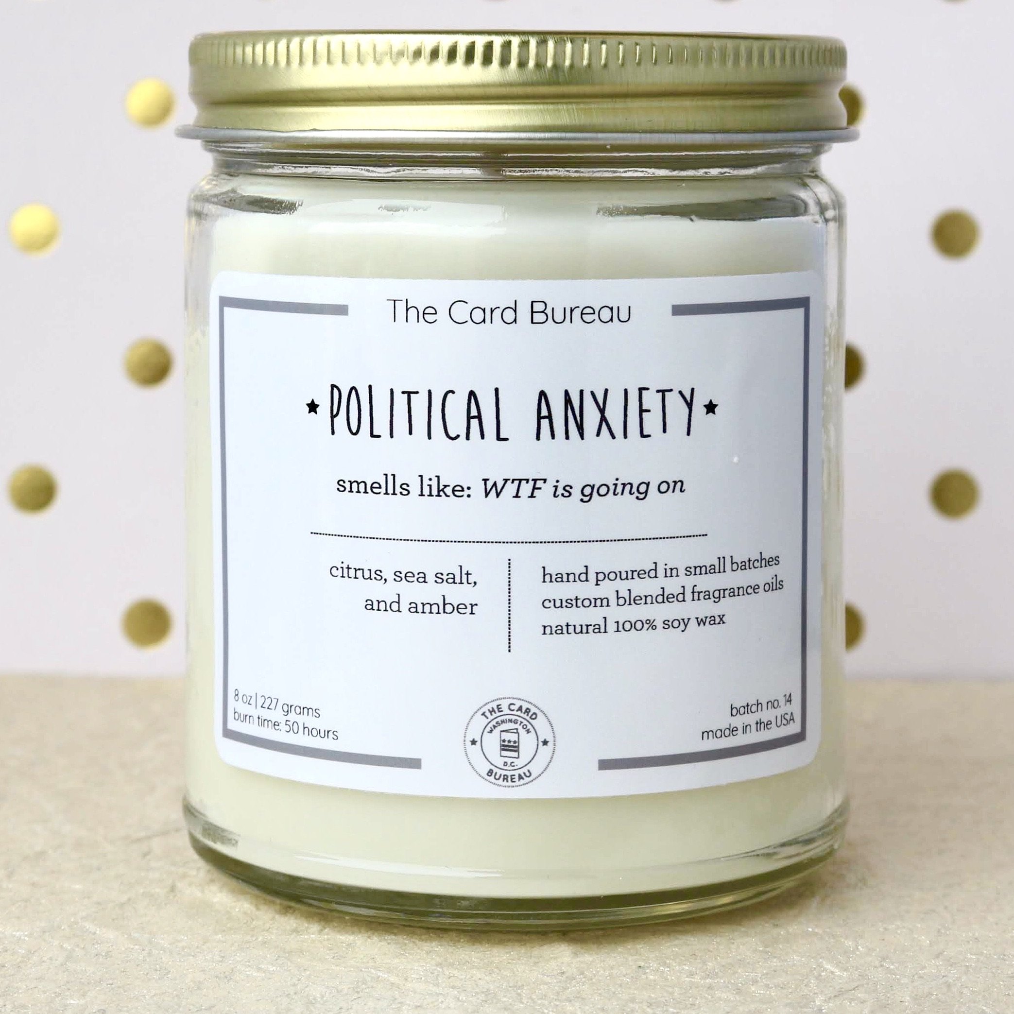 A hand-poured Political Anxiety Candle in a glass jar, featuring a citrus, sea salt, and amber scent, with a recyclable tin lid, showcasing its eco-friendly design.