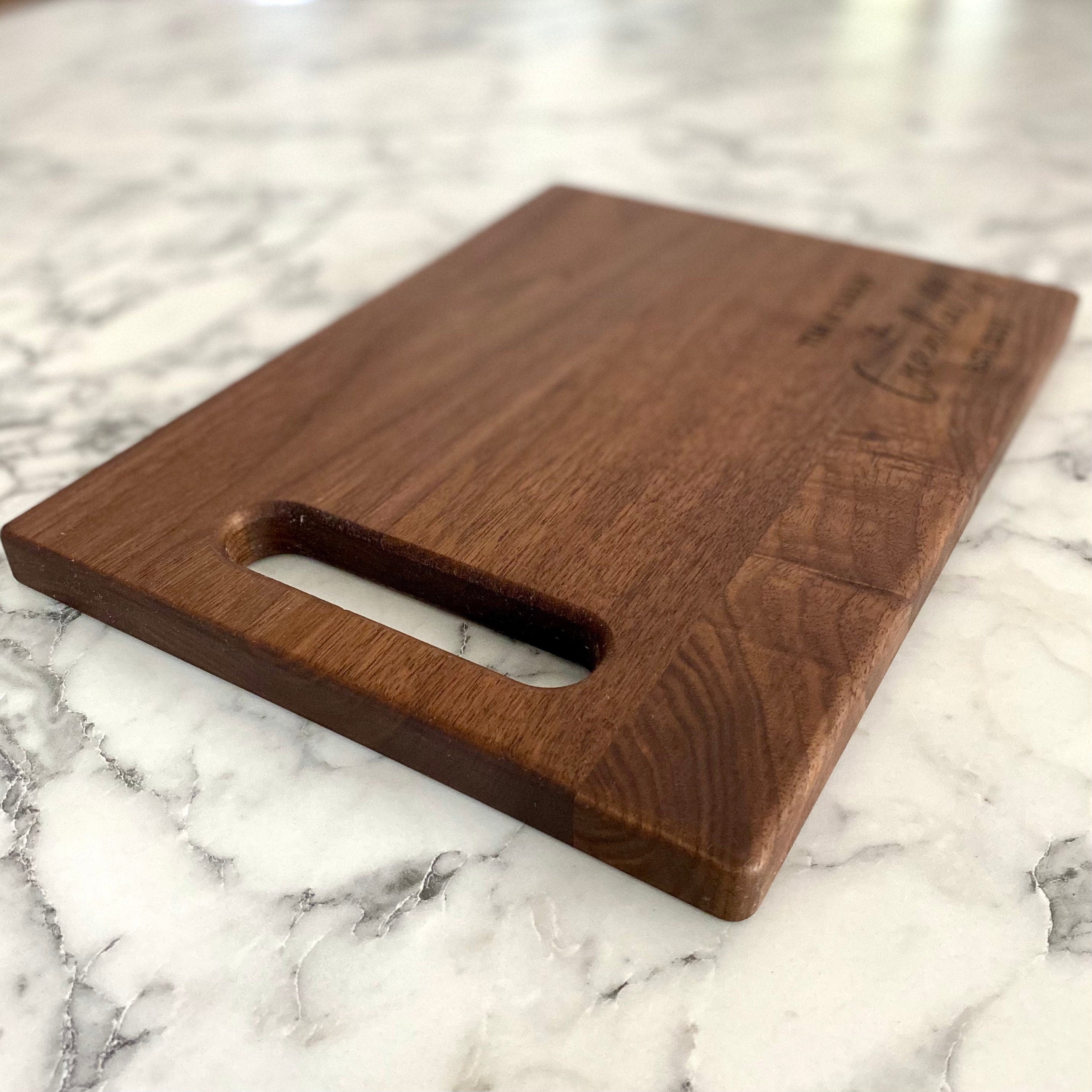 A beautifully engraved walnut wood cutting board measuring 9x12 inches, featuring a handle and custom design options.