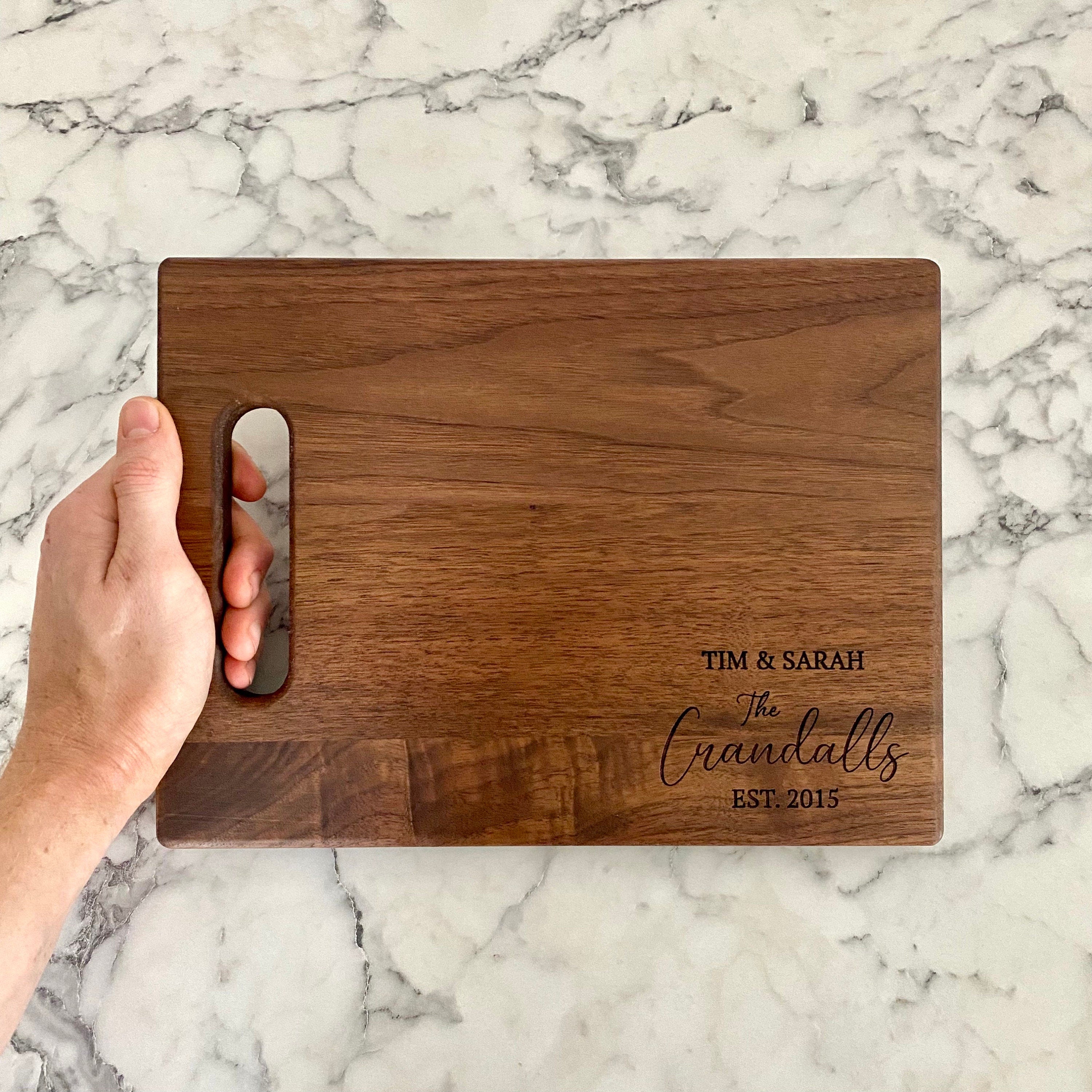 A beautifully engraved walnut wood cutting board measuring 9x12 inches, featuring a handle and custom design options.