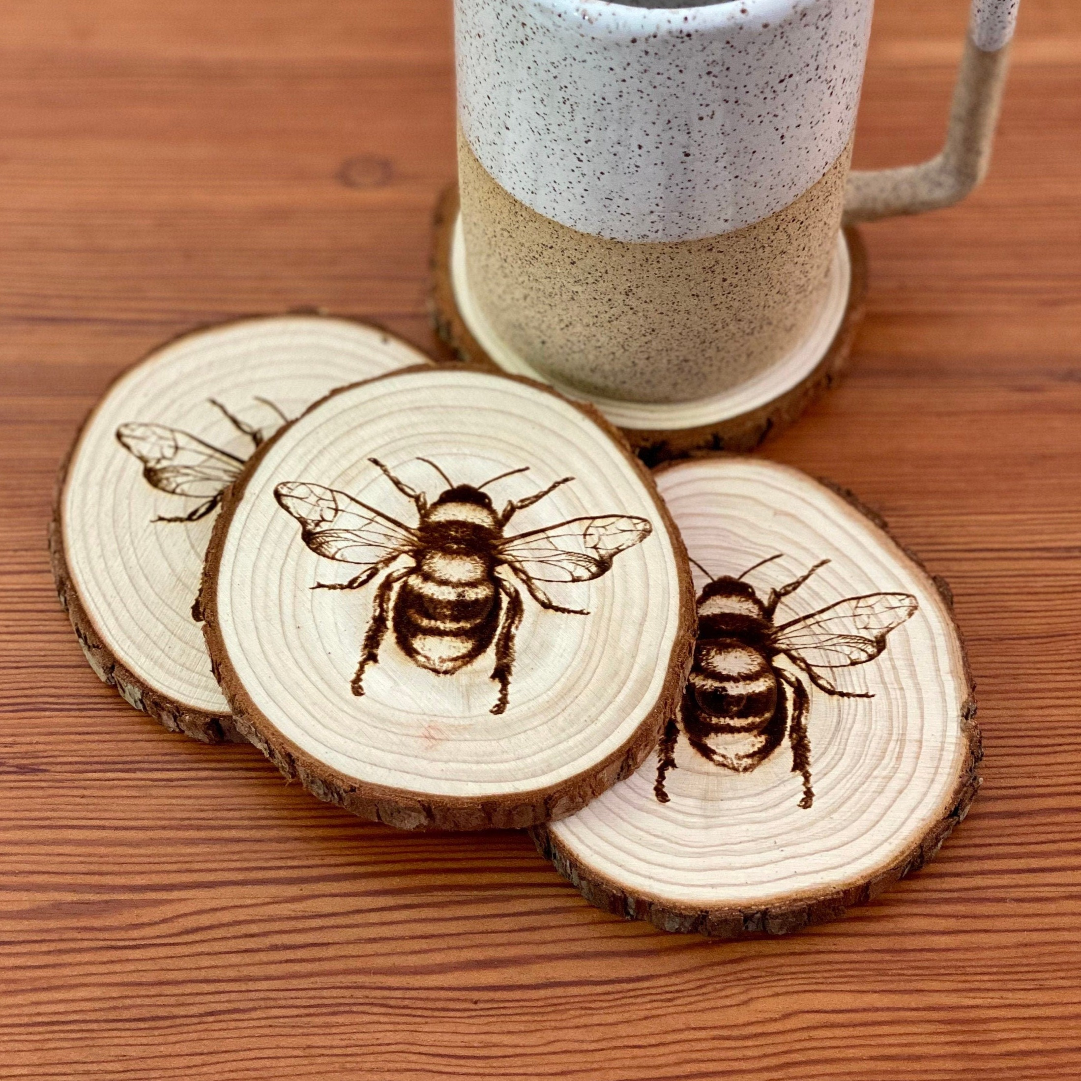 A set of four laser engraved wood coasters featuring intricate bee illustrations, showcasing their natural wood finish and unique designs.