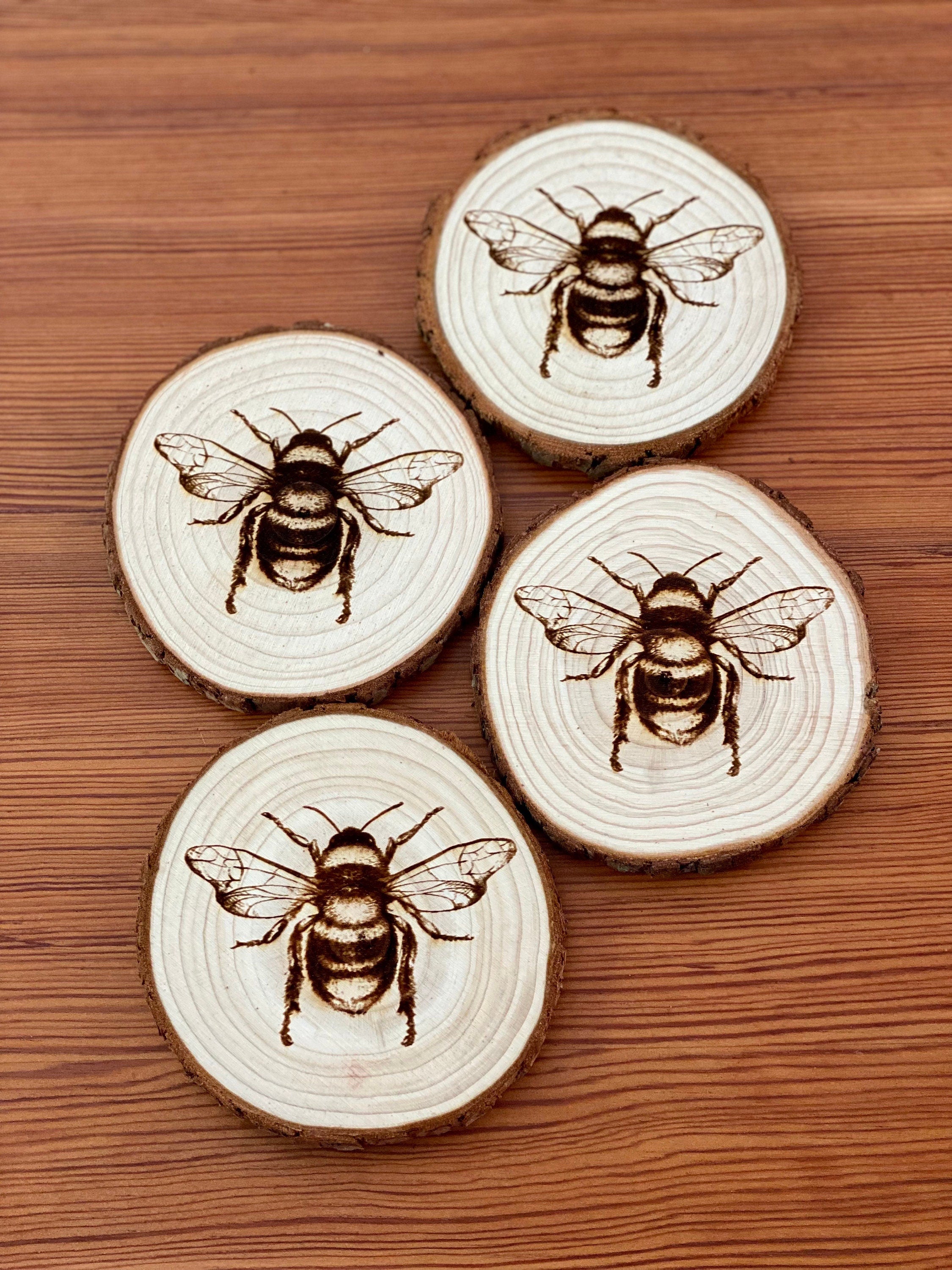 A set of four laser engraved wood coasters featuring intricate bee illustrations, showcasing their natural wood finish and unique designs.