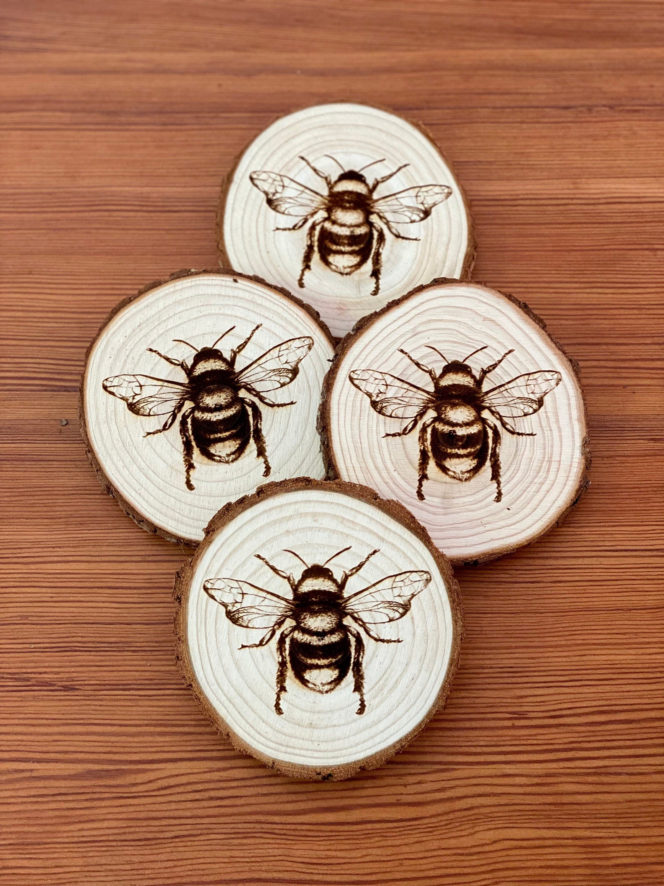 A set of four laser engraved wood coasters featuring intricate bee illustrations, showcasing their natural wood finish and unique designs.