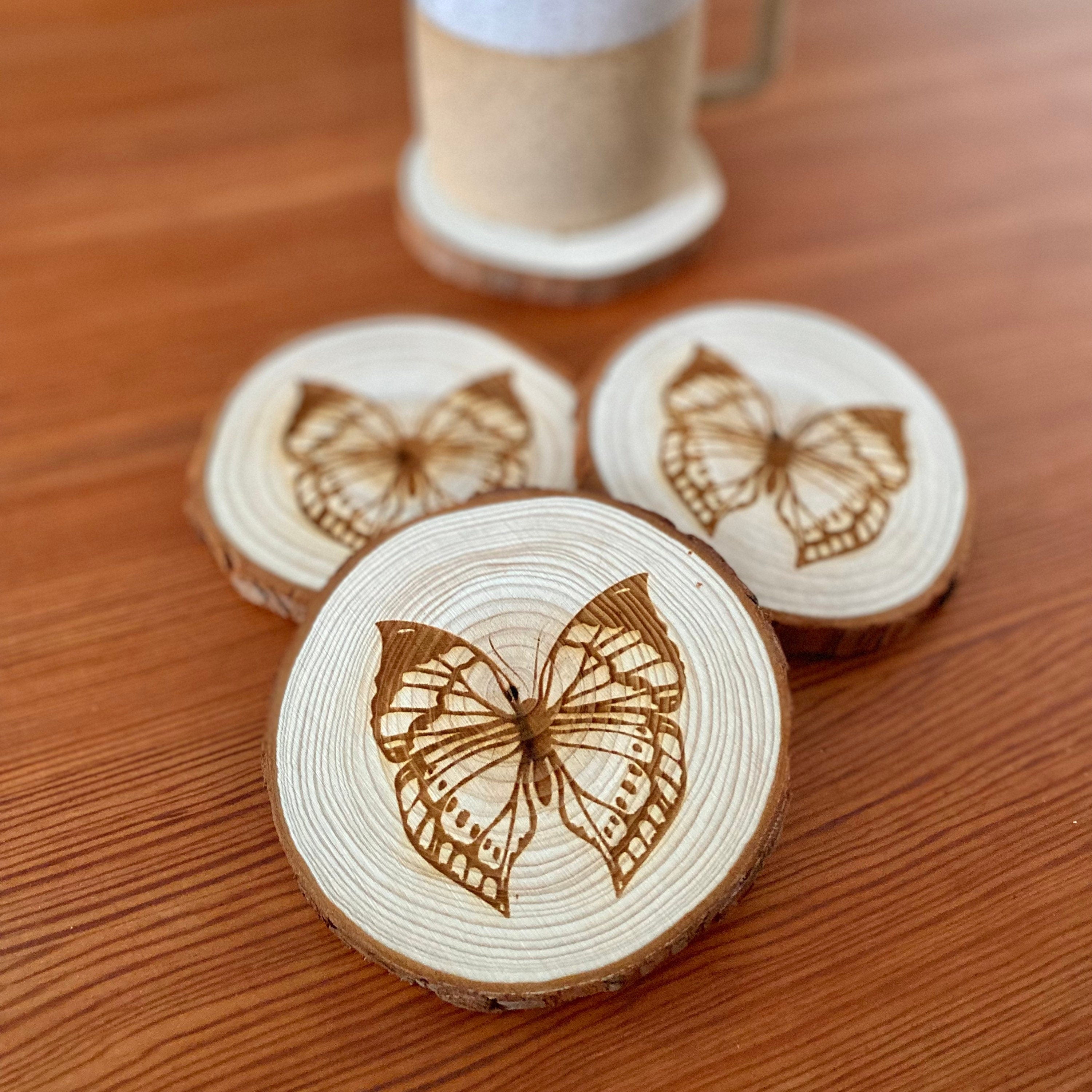 A set of four butterfly engraved wood coasters on a rustic wooden table, showcasing intricate butterfly designs.